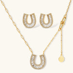 Gold-plated horseshoe necklace and earring set with baguette and round crystals arranged in geometric pattern on white background.