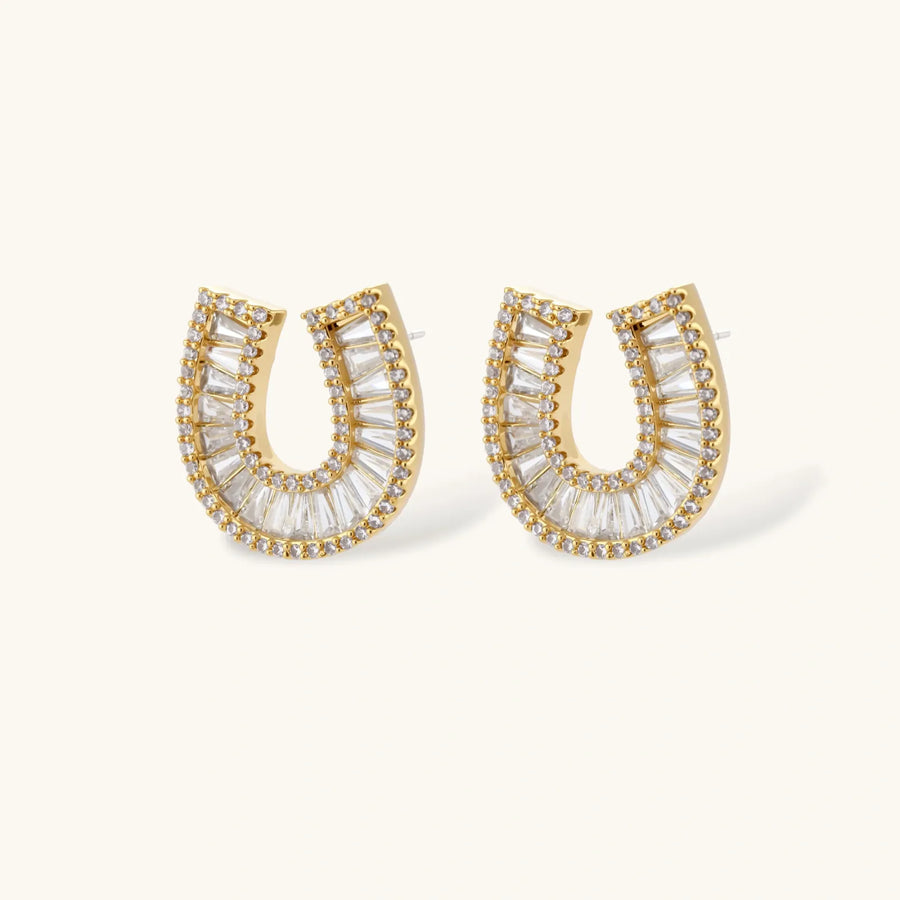 Gold-plated horseshoe necklace and earring set with baguette and round crystals arranged in geometric pattern on white background.