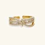 Close-up of gold-plated adjustable ring with crossing bands and sparkling zirconia stones on white background.