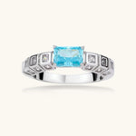 Geometric silver-plated ring with rectangular aqua cubic zirconia center and square crystal details on adjustable band.