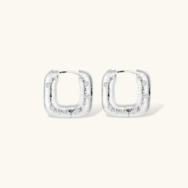 Close-up of ridged silver-plated hoop earrings with embedded crystal details on white background.
