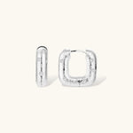 Close-up of ridged silver-plated hoop earrings with embedded crystal details on white background.