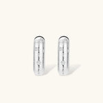 Close-up of ridged silver-plated hoop earrings with embedded crystal details on white background.