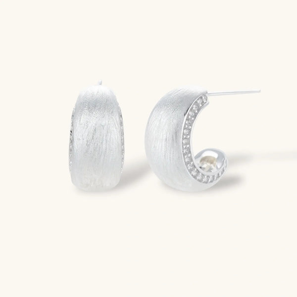 Close-up of small silver-plated hoop earrings with brushed texture and a row of sparkling zircon crystals on white background