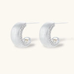 Close-up of small silver-plated hoop earrings with brushed texture and a row of sparkling zircon crystals on white background